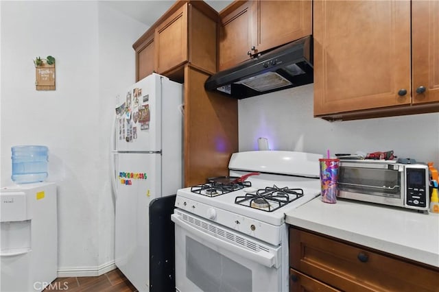 1089 E Columbia Ave, Pomona, CA 91767 - kitchen with white appliances, under cabinet range hood, brown cabinetry, light countertops, and dark wood-style flooring