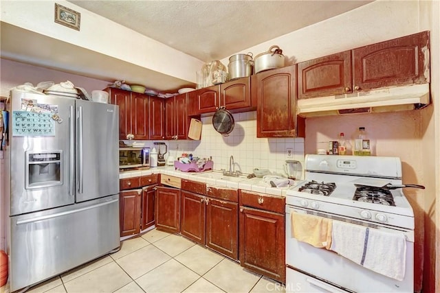 1132 E 53rd St, Los Angeles, CA 90011 - kitchen featuring stainless steel appliances, under cabinet range hood, light tile patterned floors, tile countertops, and decorative backsplash