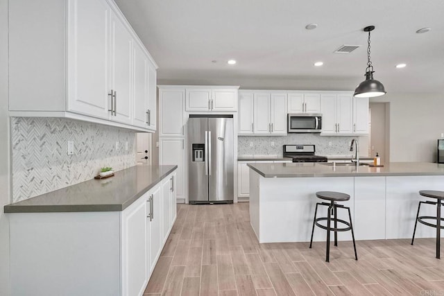 678 Gemstone Dr, San Marcos, CA 92078 - kitchen featuring stainless steel appliances, a kitchen bar, backsplash, light wood-style floors, and white cabinets