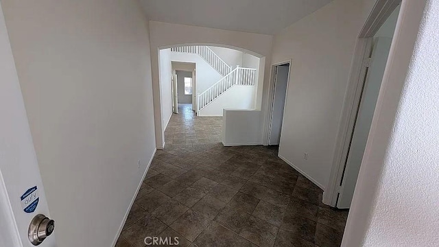 3929 Albillo, Perris, CA 92571 - hallway featuring arched walkways, baseboards, dark stone finish flooring, and stairway