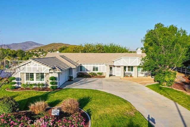 36884 Hidden Trail Ct, Winchester, CA 92596 - tudor house with concrete driveway, an attached garage, a front yard, and a mountain view