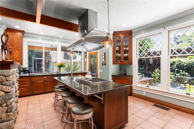 337 S Center St, Redlands, CA 92373 - kitchen with island exhaust hood, light tile patterned floors, stainless steel gas stovetop, dark countertops, and brown cabinetry