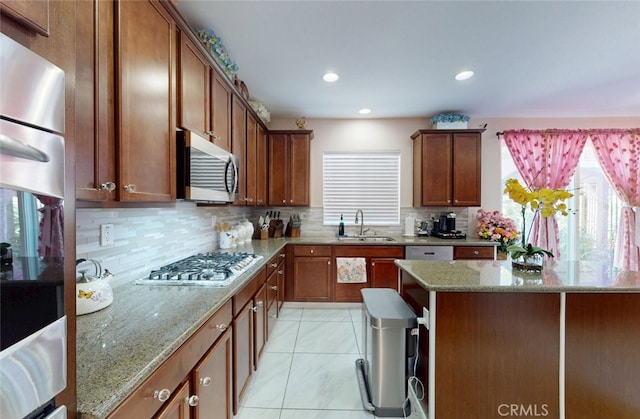 25664 Red Hawk Rd, Corona, CA 92883 - kitchen with stainless steel appliances, a sink, light stone counters, decorative backsplash, and brown cabinetry