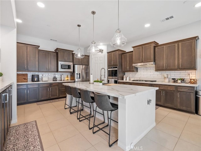 17028 Ta Ki Pi Rd, Apple Valley, CA 92307 - kitchen featuring appliances with stainless steel finishes, backsplash, a kitchen breakfast bar, a kitchen island with sink, and dark brown cabinetry