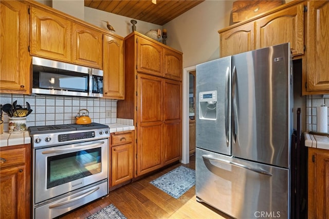 1760 Stuart St, Cambria, CA 93428 - kitchen with appliances with stainless steel finishes, tile counters, decorative backsplash, dark wood-style floors, and brown cabinets