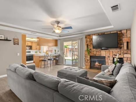 11191 Baker Ln, Riverside, CA 92505 - living area featuring a ceiling fan, a stone fireplace, baseboards, a raised ceiling, and wood finished floors