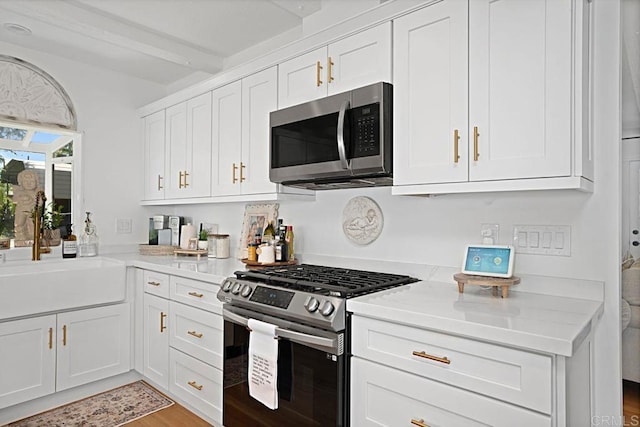 17030 Grand Ave, Lake Elsinore, CA 92530 - kitchen with appliances with stainless steel finishes, light countertops, white cabinetry, light wood-style flooring, and beam ceiling