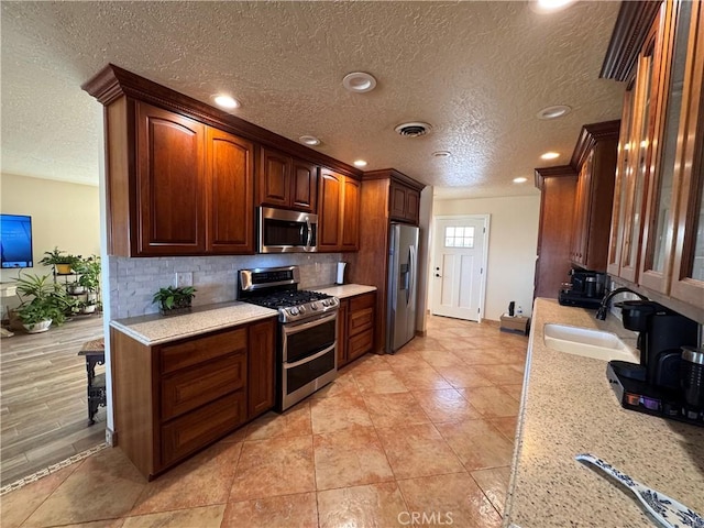 27568 Linda Vista Rd, Barstow, CA 92311 - kitchen featuring appliances with stainless steel finishes, a textured ceiling, a sink, tasteful backsplash, and glass insert cabinets