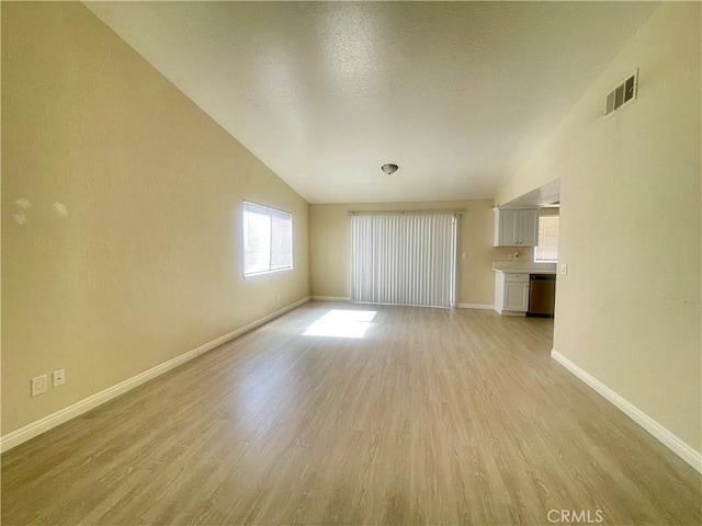 1305 Herzel Ave, Lancaster, CA 93535 - unfurnished living room featuring light wood finished floors, vaulted ceiling, baseboards, and a textured ceiling