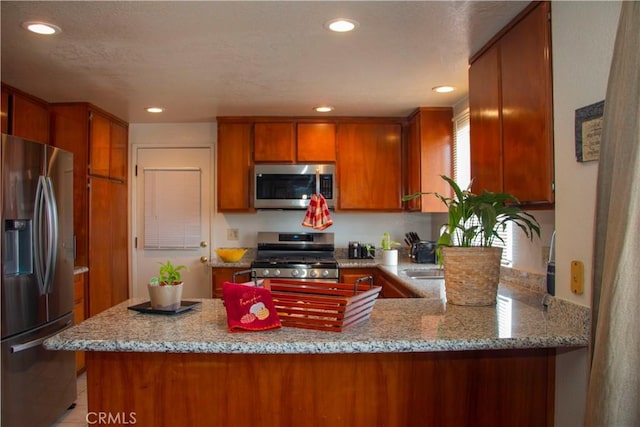 916 E 65th St Unit 3, Inglewood, CA 90302 - kitchen with appliances with stainless steel finishes, brown cabinetry, a peninsula, recessed lighting, and light stone counters