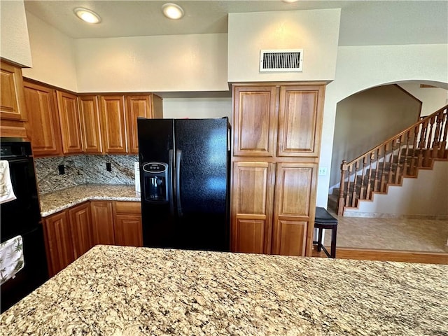 915 Beach Dr, Needles, CA 92363 - kitchen featuring black fridge with ice dispenser, light stone counters, brown cabinetry, wood finished floors, and tasteful backsplash
