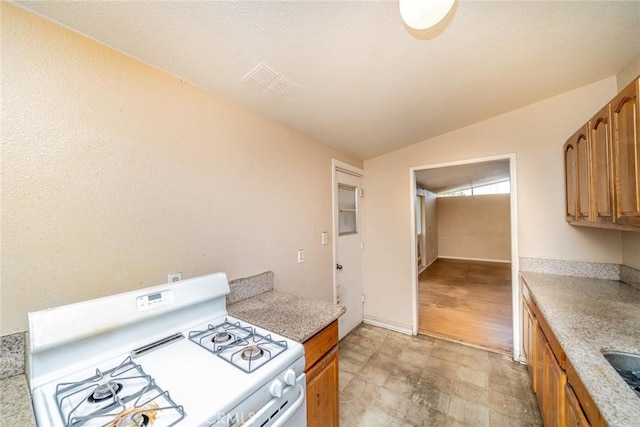 17941 E Payson St, Azusa, CA 91702 - kitchen with white range with gas cooktop, lofted ceiling, brown cabinets, light countertops, and light flooring