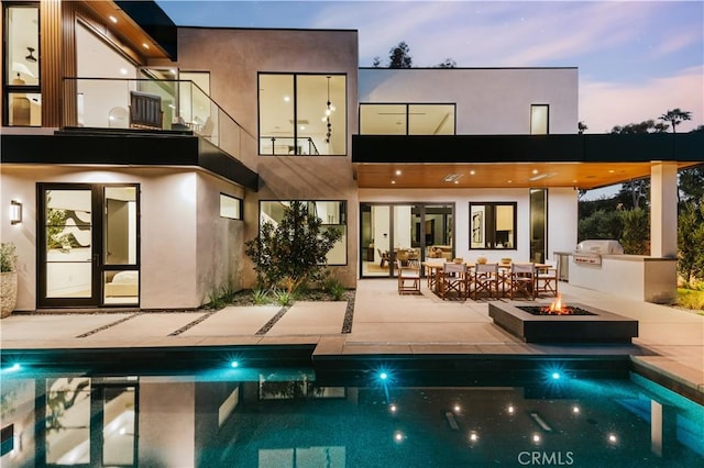 2321 Mesa Dr, Newport Beach, CA 92660 - back of house at dusk with exterior kitchen, a balcony, a patio, a fire pit, and an outdoor pool