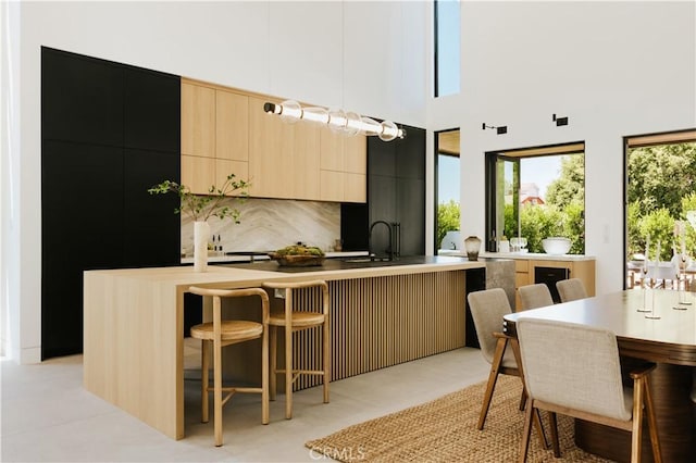 2321 Mesa Dr, Newport Beach, CA 92660 - kitchen featuring modern cabinets, a kitchen island with sink, a sink, light brown cabinetry, and decorative backsplash