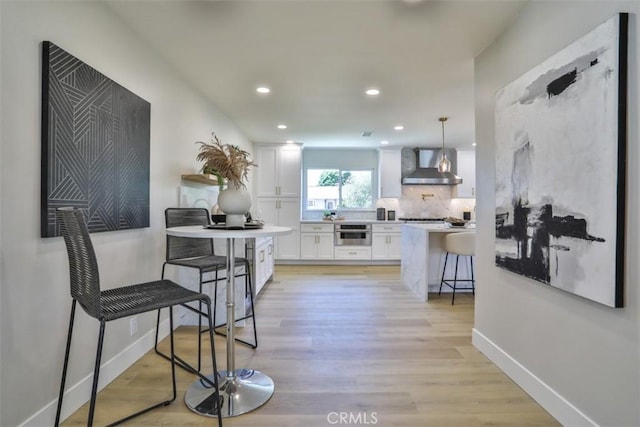 13181 Olympia Way N, Tustin, CA 92705 - kitchen featuring wall chimney range hood, white cabinetry, a kitchen breakfast bar, light wood-style floors, and recessed lighting
