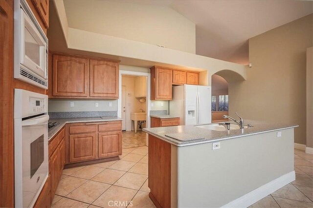 24347 Silver Bullet Way, Murrieta, CA 92562 - kitchen with white appliances, light tile patterned floors, a sink, a center island with sink, and arched walkways