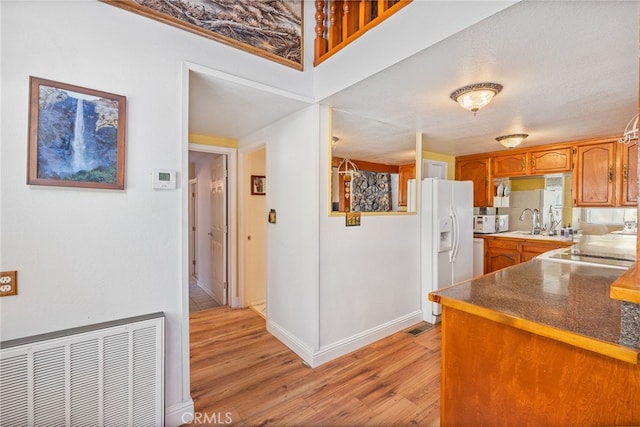 37731 Shoreline Dr, Bass Lake, CA 93604 - kitchen featuring white fridge with ice dispenser, light wood-type flooring, brown cabinetry, a sink, and baseboards