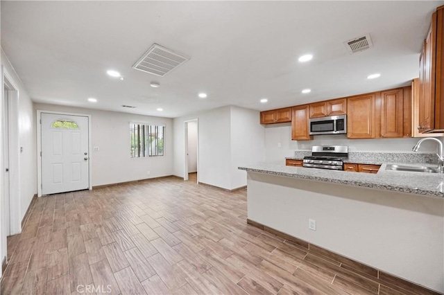 8426 Orange St, Downey, CA 90242 - kitchen featuring appliances with stainless steel finishes, brown cabinets, recessed lighting, light wood-type flooring, and light stone countertops