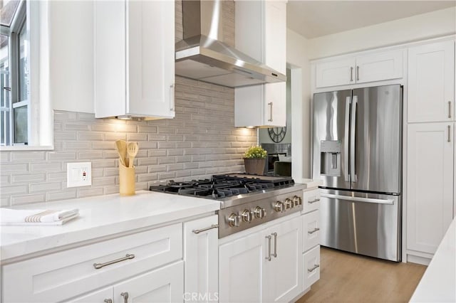 8426 Orange St, Downey, CA 90242 - kitchen featuring stainless steel appliances, wall chimney range hood, white cabinets, backsplash, and light wood-type flooring