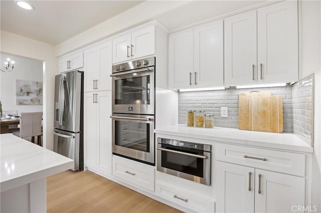 8426 Orange St, Downey, CA 90242 - kitchen featuring stainless steel appliances, white cabinets, light countertops, light wood-type flooring, and decorative backsplash