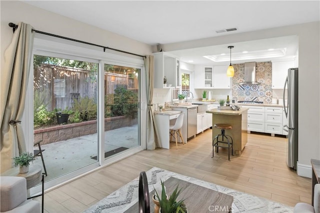 61 Bridgeport, Irvine, CA 92620 - kitchen with wall chimney range hood, appliances with stainless steel finishes, a tray ceiling, white cabinetry, and light wood-style floors