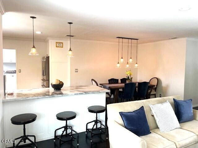 10456 Pomering Rd, Downey, CA 90241 - kitchen with stainless steel fridge, ornamental molding, a kitchen breakfast bar, a peninsula, and hanging light fixtures