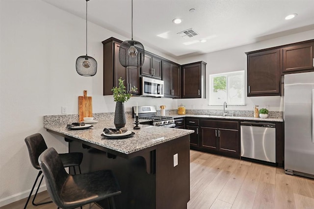 170 Montage Dr, Merced, CA 95348 - kitchen with appliances with stainless steel finishes, light stone counters, dark brown cabinetry, a peninsula, and a kitchen breakfast bar
