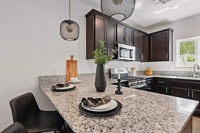 170 Montage Dr, Merced, CA 95348 - kitchen with appliances with stainless steel finishes, a sink, light stone counters, a peninsula, and dark brown cabinets