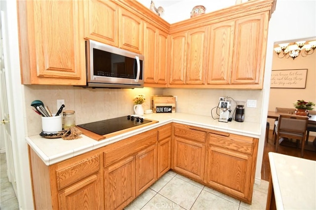 8250 Cataba Rd, Oak Hills, CA 92344 - kitchen featuring stainless steel microwave, black electric cooktop, light tile patterned floors, tile countertops, and tasteful backsplash