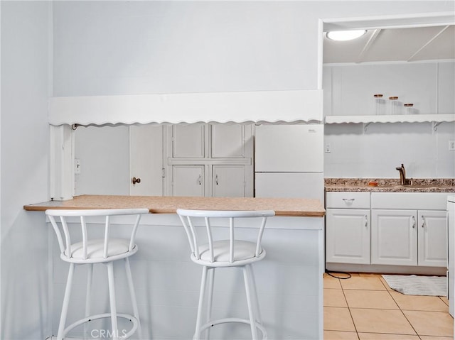1040 Flora St, Barstow, CA 92311 - kitchen featuring freestanding refrigerator, a kitchen bar, a sink, light tile patterned floors, and white cabinetry