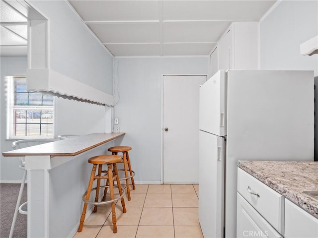 1040 Flora St, Barstow, CA 92311 - kitchen featuring a kitchen bar, freestanding refrigerator, white cabinets, light tile patterned floors, and light countertops