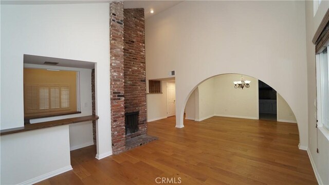 24530 Breckenridge Pl, Newhall, CA 91321 - unfurnished living room with a towering ceiling, a brick fireplace, wood finished floors, a chandelier, and baseboards