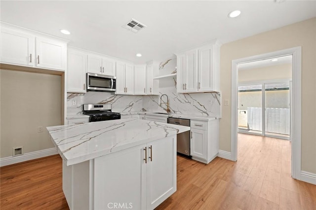 2101 W 76th St, Los Angeles, CA 90047 - kitchen with stainless steel appliances, a sink, white cabinets, light wood-style floors, and tasteful backsplash