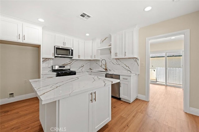 2101 W 76th St, Los Angeles, CA 90047 - kitchen featuring stainless steel appliances, white cabinetry, light wood-style floors, decorative backsplash, and a kitchen island