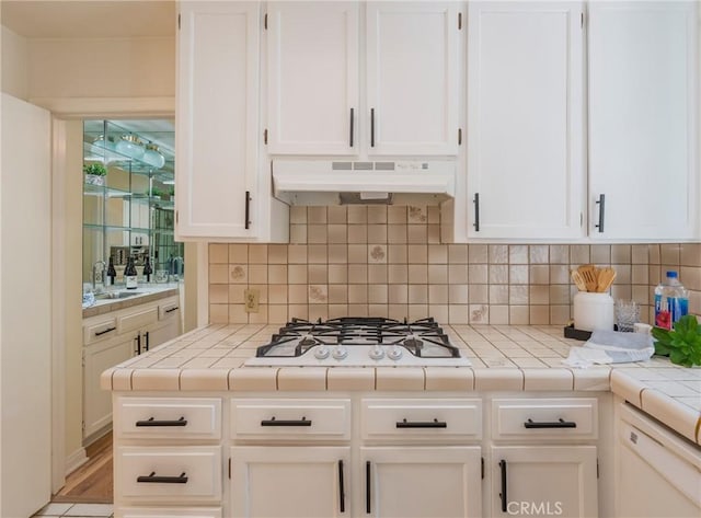 1375 Kelton Ave Unit 104, Los Angeles, CA 90024 - kitchen with under cabinet range hood, white appliances, a sink, white cabinets, and tasteful backsplash