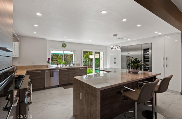 27773 Hidden Trail Rd, Laguna Hills, CA 92653 - kitchen featuring appliances with stainless steel finishes, modern cabinets, light marble finish flooring, recessed lighting, and a breakfast bar area