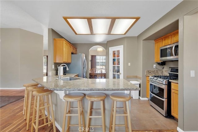 9275 Verdugo Ave, Hesperia, CA 92345 - kitchen with appliances with stainless steel finishes, a sink, arched walkways, a peninsula, and light stone countertops