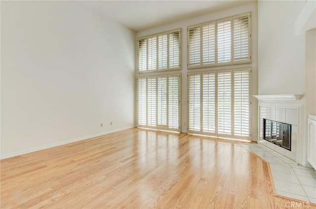 6052 Shadowbrook Cir, Huntington Beach, CA 92648 - unfurnished living room featuring a tile fireplace, plenty of natural light, wood finished floors, a towering ceiling, and baseboards