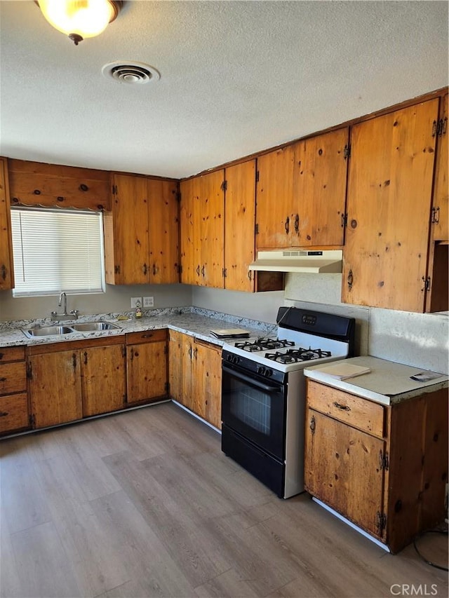 6025 Florence St, Riverside, CA 92504 - kitchen featuring gas stove, under cabinet range hood, light wood finished floors, brown cabinetry, and a textured ceiling