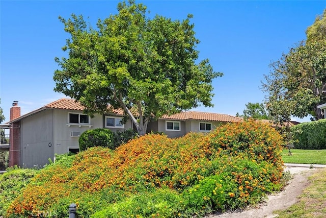 2117 Via Puerta Unit A, Laguna Woods, CA 92637 - view of property hidden behind natural elements with a tiled roof, stucco siding, and a chimney