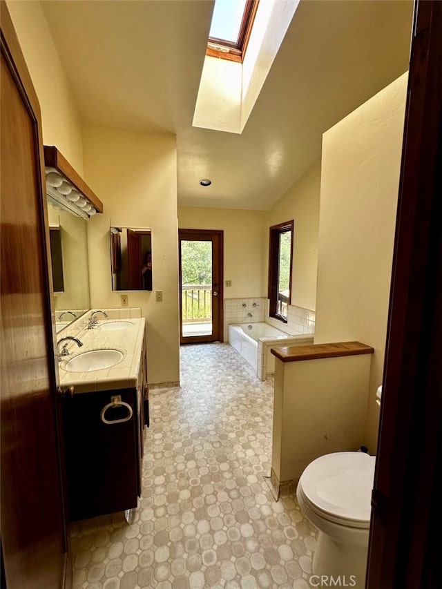 50771 Woodside Ln, Oakhurst, CA 93644 - bathroom featuring a skylight, toilet, double vanity, a bath, and lofted ceiling