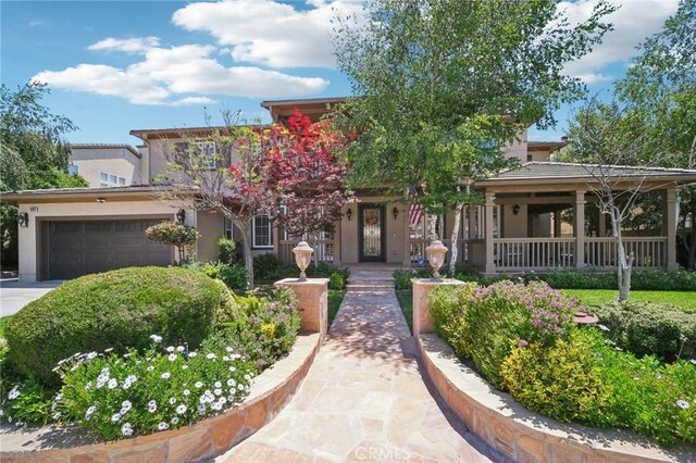 25422 Magnolia Ln, Stevenson Ranch, CA 91381 - view of property hidden behind natural elements featuring stucco siding, an attached garage, driveway, and covered porch