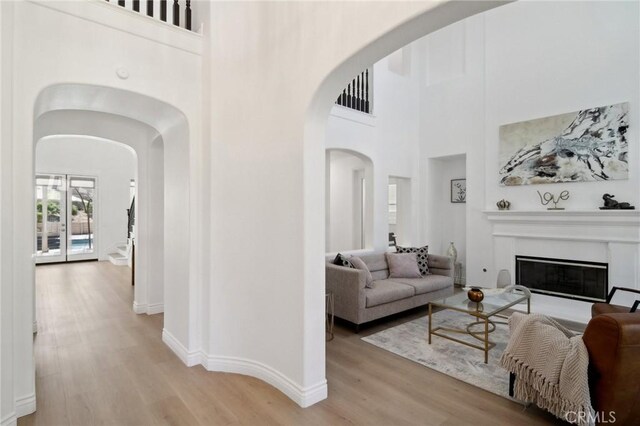 25422 Magnolia Ln, Stevenson Ranch, CA 91381 - living room with arched walkways, light wood finished floors, a glass covered fireplace, baseboards, and a towering ceiling
