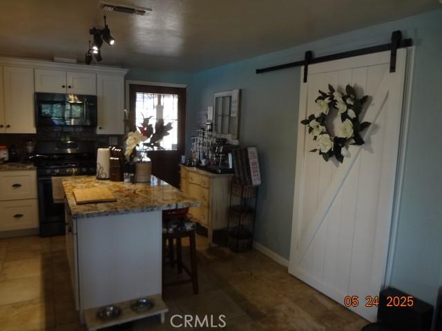5475 Wilkinson Ave, Clearlake, CA 95422 - kitchen with black gas range oven, a barn door, light stone countertops, a kitchen island, and white cabinetry
