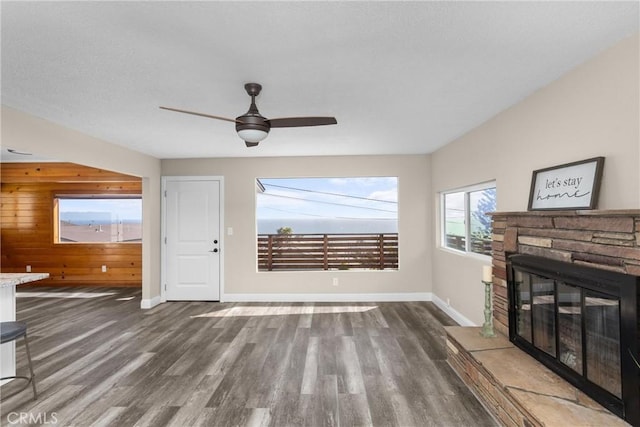 833 Park Ave, Cayucos, CA 93430 - unfurnished living room featuring wood finished floors, wood walls, baseboards, a stone fireplace, and ceiling fan