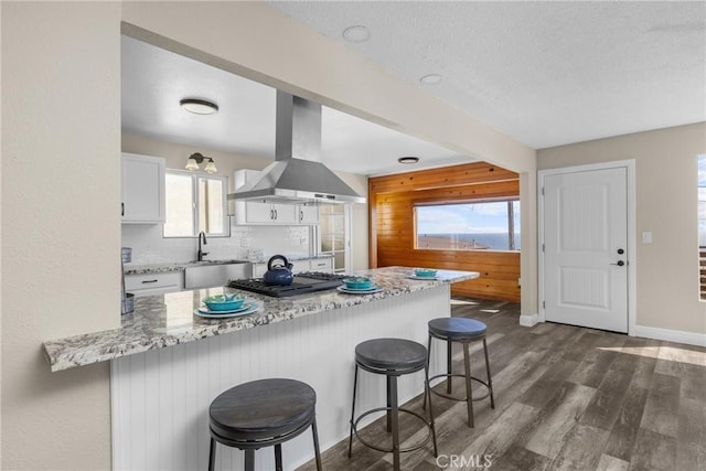 833 Park Ave, Cayucos, CA 93430 - kitchen featuring wall chimney exhaust hood, a sink, a breakfast bar area, white cabinetry, and a peninsula