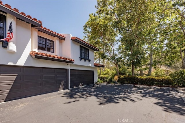 34101 Via California Unit 12, San Juan Capistrano, CA 92675 - view of front facade featuring a tiled roof, driveway, a garage, and stucco siding