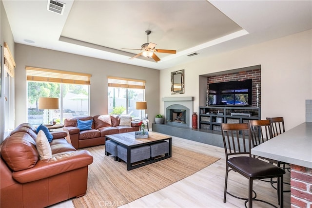 23840 Costa Mesa Way, Murrieta, CA 92562 - living room featuring a tray ceiling, a ceiling fan, a fireplace with raised hearth, and light wood-type flooring