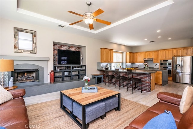 23840 Costa Mesa Way, Murrieta, CA 92562 - living room featuring ceiling fan, light wood finished floors, a raised ceiling, recessed lighting, and a high end fireplace