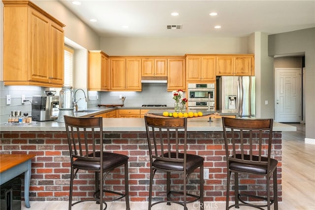 23840 Costa Mesa Way, Murrieta, CA 92562 - kitchen featuring stainless steel appliances, a sink, under cabinet range hood, decorative backsplash, and light wood-style floors